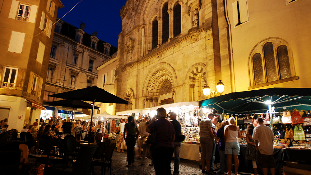 Ambiance authentique d’un marché ardéchois en été Étal de fruits et légumes frais sur un marché local en Ardèche, avec des passants en arrière-plan