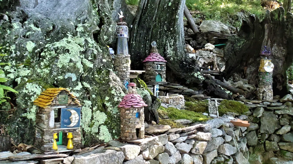 Village d’artisanat miniature Présentation de plusieurs maquettes en pierre sur des supports en bois, dont un moulin à vent miniature et une pancarte "Pépé Labuche agent immobilier".