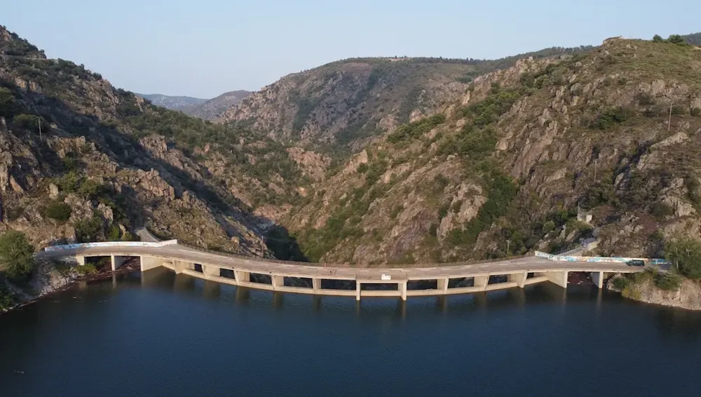 vue-aerienne-rapprochee-barrage-lac-villefort Vue aérienne rapprochée du barrage arqué du lac de Villefort, traversant une gorge rocheuse profonde. Le sentier de randonnée passe sur le sommet de l'ouvrage.